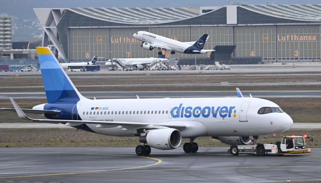 Während eine Maschine der Lufthansa startet, wird ein Passagierflugzeug der Discover Airlines am Frankfurter Flughafen von einem Schlepper gezogen.