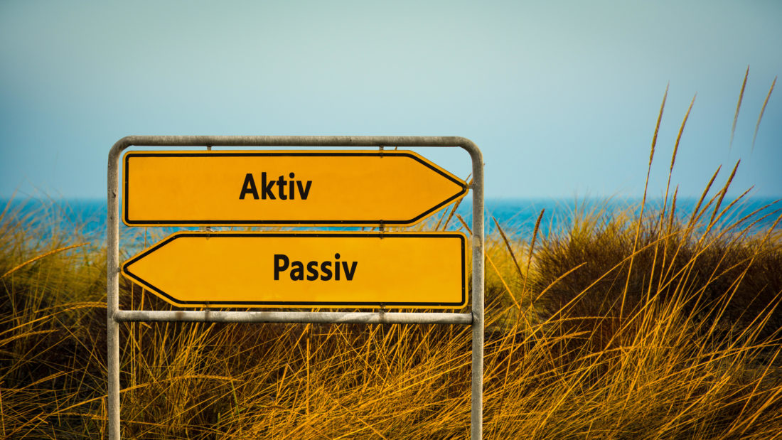 An image with a signpost pointing in two different directions in German. One direction points to Active, the other points to Passive. Aktiv - Passiv - Symbolbild