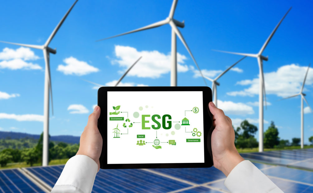 Person mit Laptop, darauf ESG-Daten – im Hintergrund Windräder, Solarpanels und Wald.